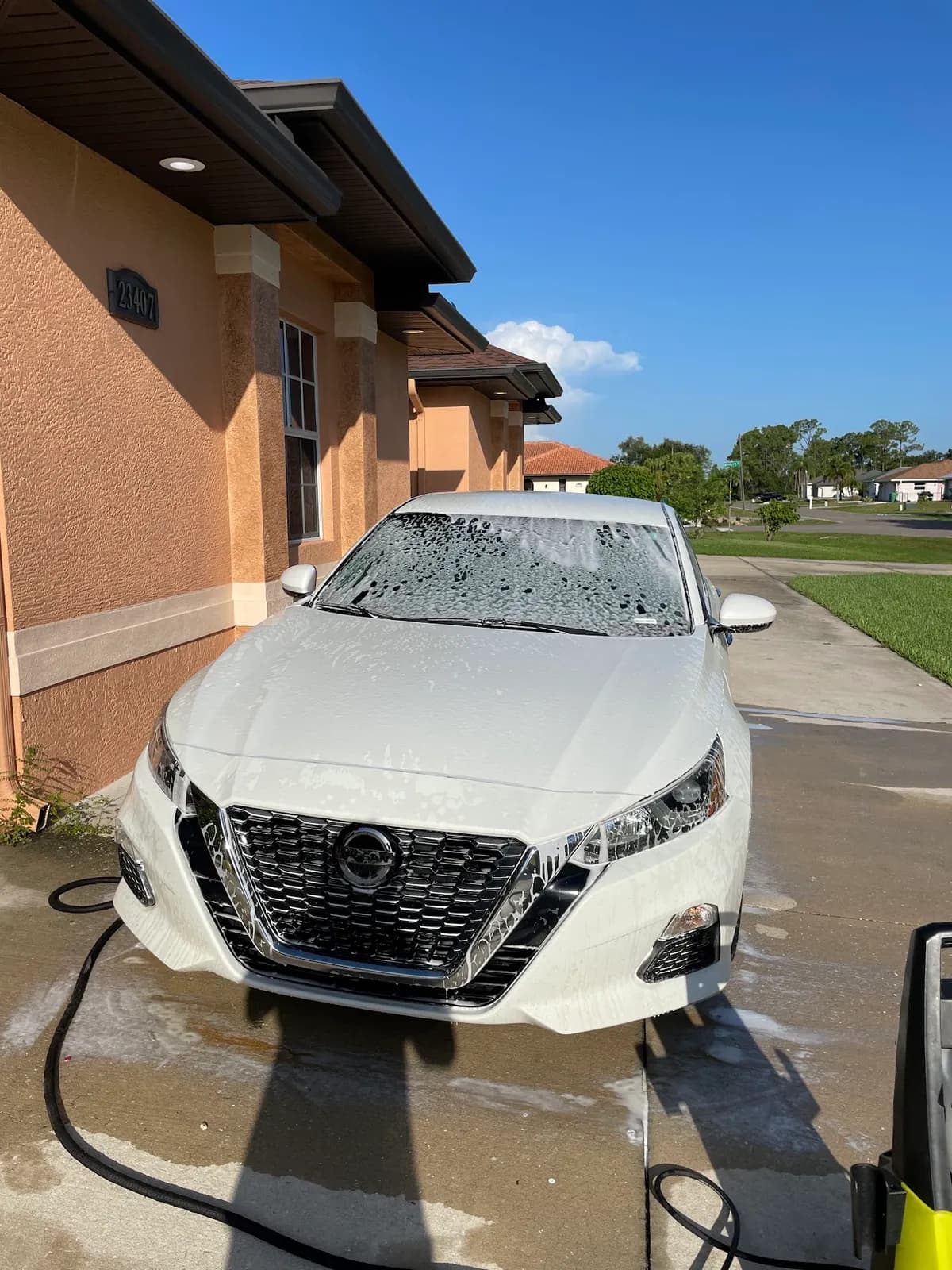 Mobile car detailing in action — white Nissan covered in foam during hand wash at customer home in North Port, FL by Sansanich Car Detailing